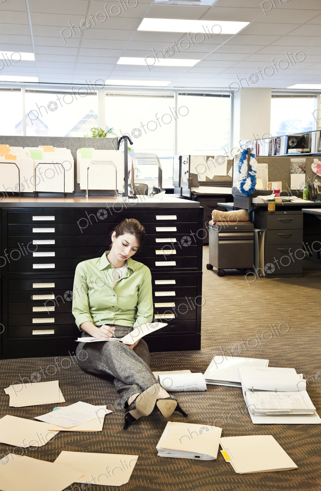 A young Caucasian businesswoman sitting on the floor of her office going over paperwork.
