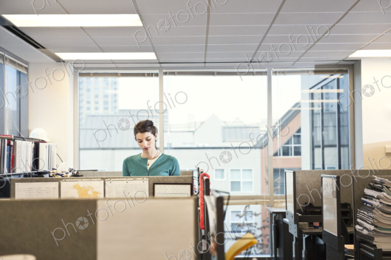 A young Caucasian businesswoman working in her cubicle in a corporate office.
