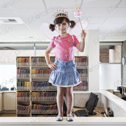 A young Caucasian girl dressed up as a fairy standing on a reception desk in a dental…
