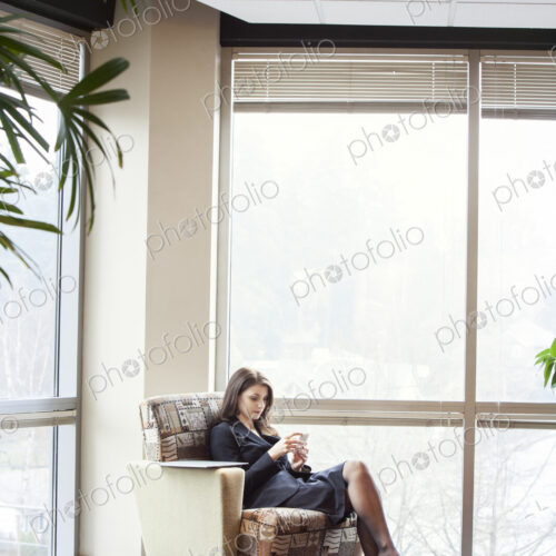 A young Caucasian woman checking her phone in an office lobby.