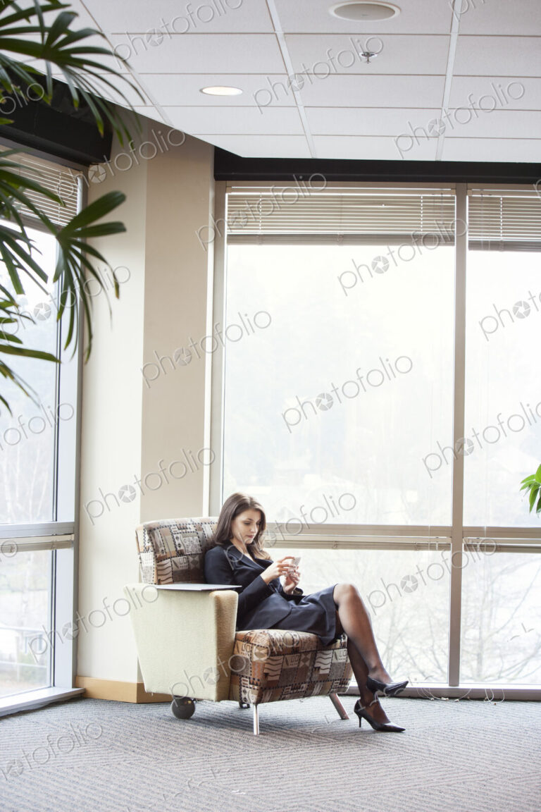 A young Caucasian woman checking her phone in an office lobby.