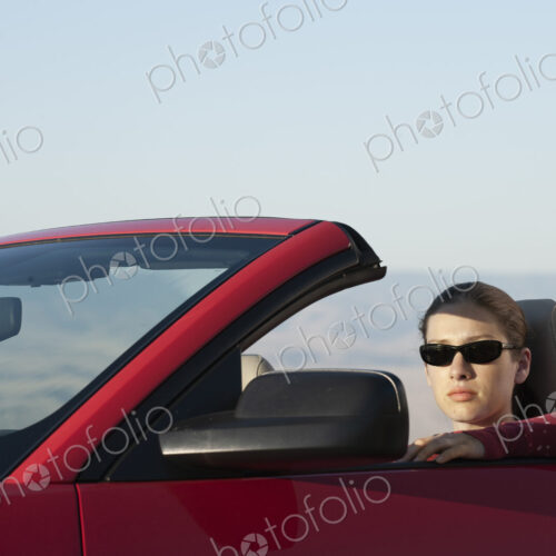A young Caucasian woman in a convertible sports car.