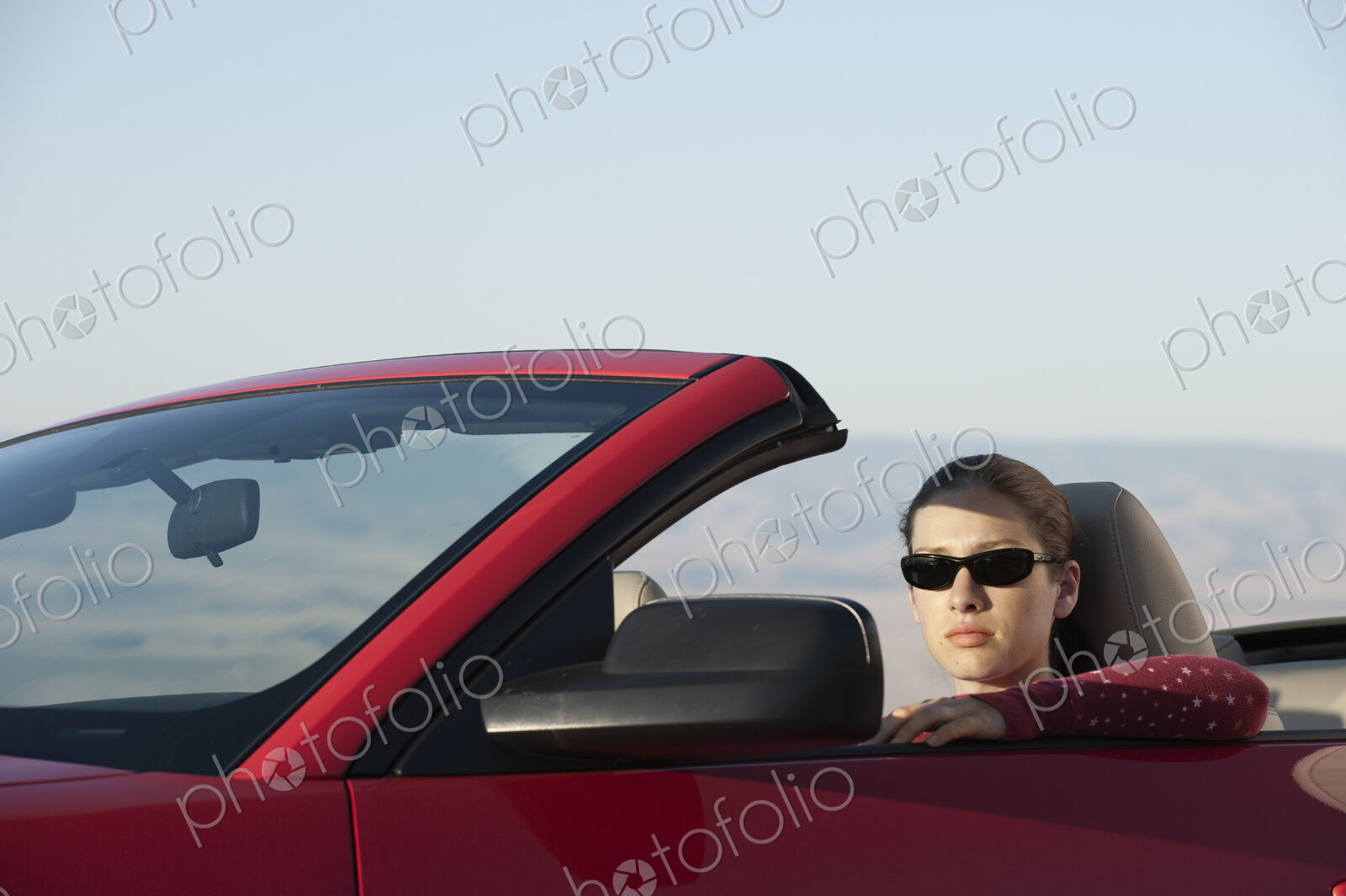 A young Caucasian woman in a convertible sports car.