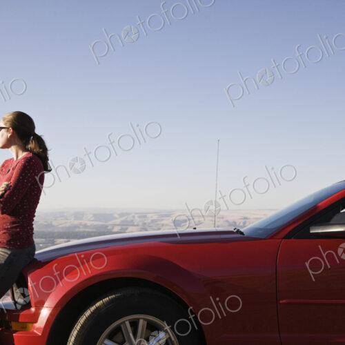 A young Caucasian woman leaning on her convertible sports car at a rest stop. A young Caucasian woman leaning on her convertible sports car at a rest stop.