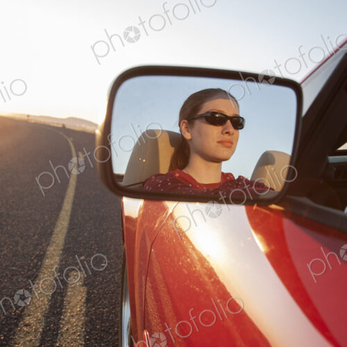 A young Caucasian woman reflected in side mirror of a convertible sports car on the…