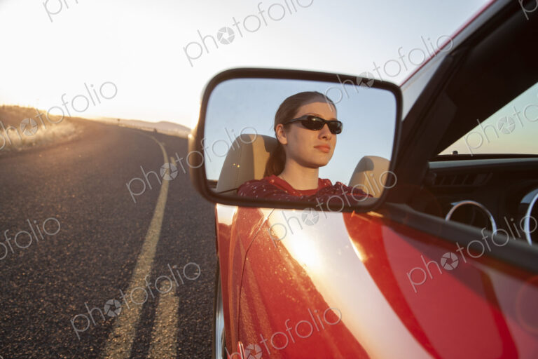 A young Caucasian woman reflected in side mirror of a convertible sports car on the…