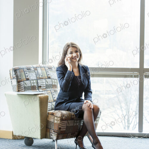 A young Caucasian woman talking on her phone in an office lobby.