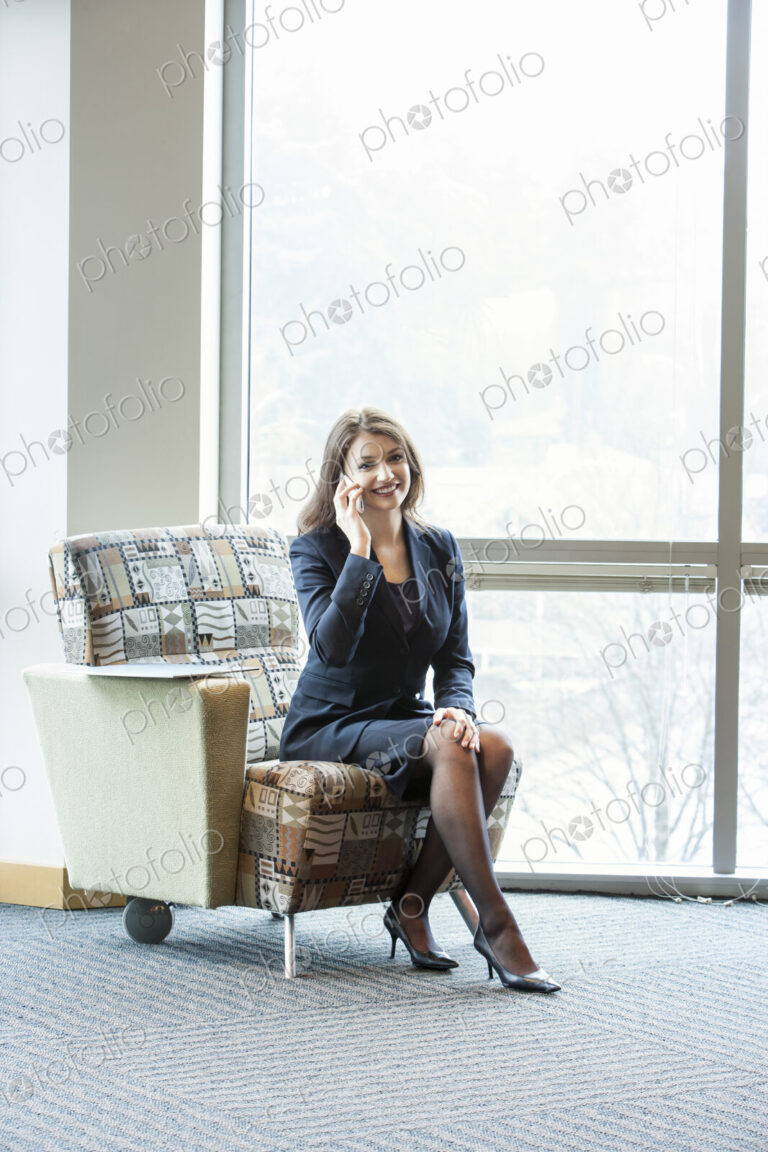 A young Caucasian woman talking on her phone in an office lobby.