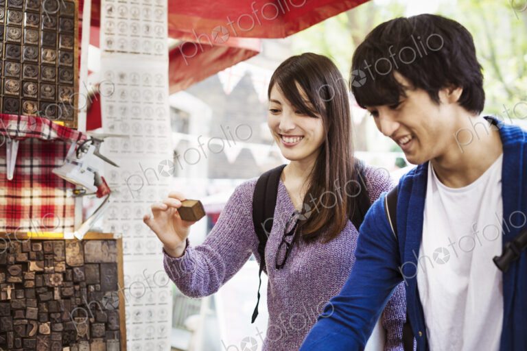 A young Japanese couple, man and woman at a souvenir street stall looking at printing…