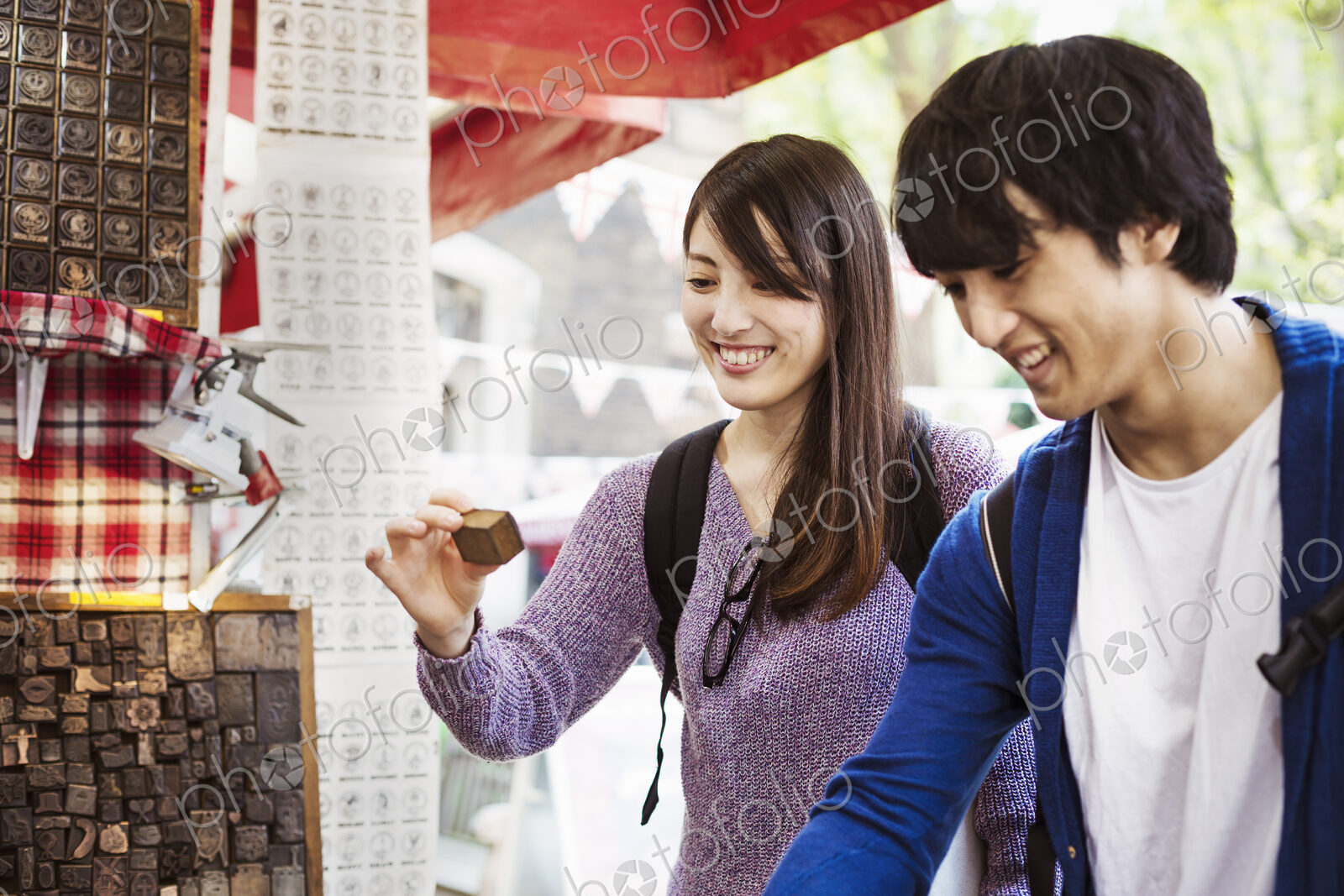 A young Japanese couple, man and woman at a souvenir street stall looking at printing…