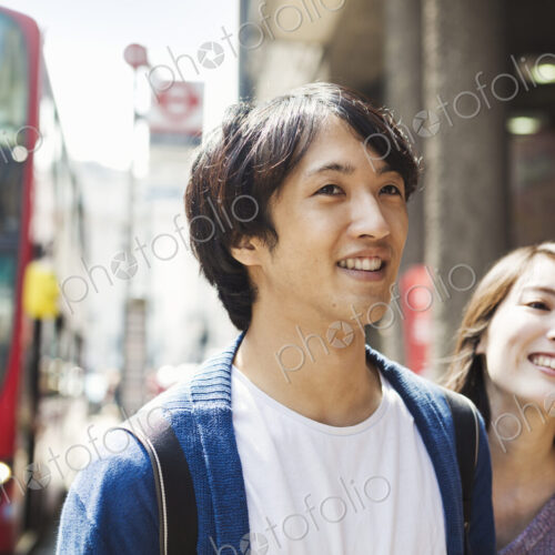 A young Japanese woman and man, a couple on the street in London, a red bus in the…