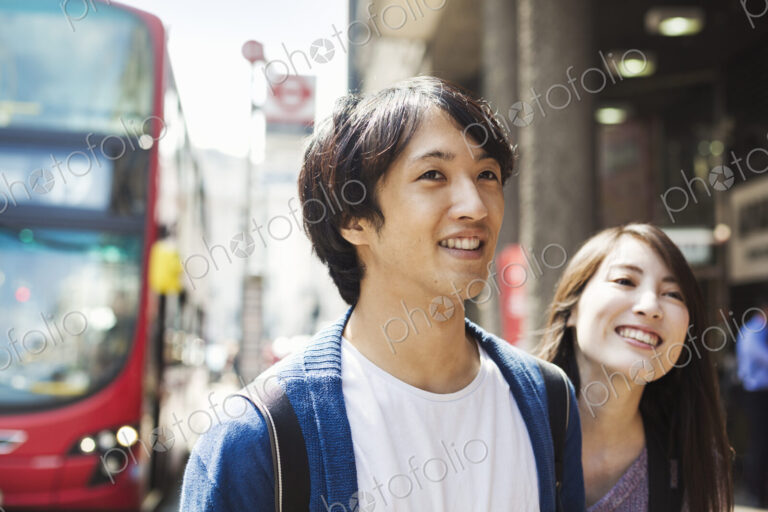 A young Japanese woman and man, a couple on the street in London, a red bus in the…
