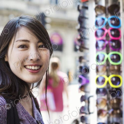 A young Japanese woman smiling at the camera, by a sunglasses display.