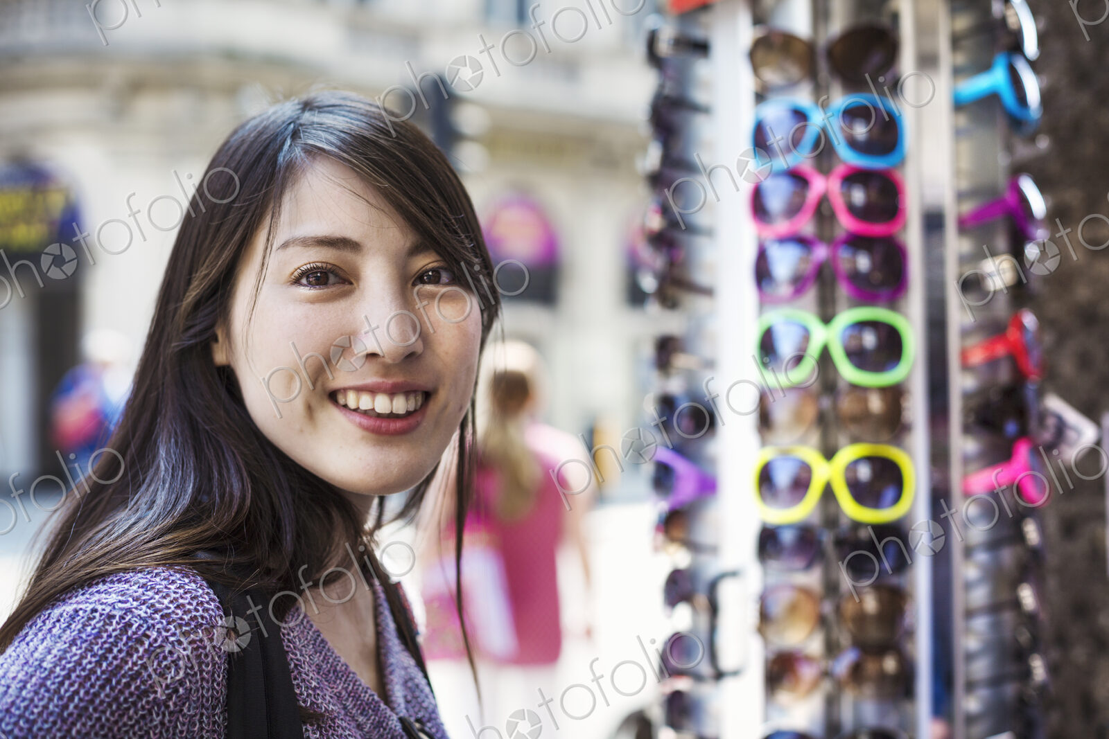 A young Japanese woman smiling at the camera, by a sunglasses display.