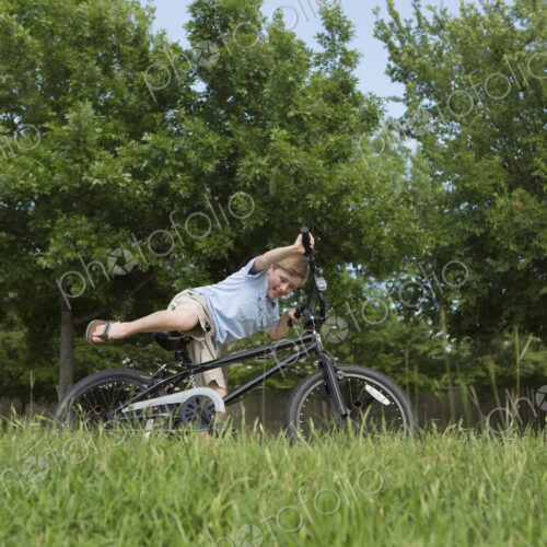 A young boy falling off his bicycle, overbalancing in a grassy field. A young boy falling off his bicycle, overbalancing in a grassy field.