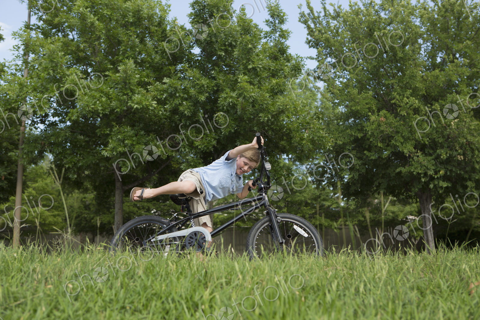 A young boy falling off his bicycle, overbalancing in a grassy field.