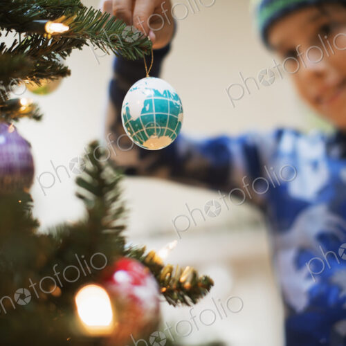 A young boy holding Christmas ornaments and placing them on the Christmas tree. A young boy holding Christmas ornaments and placing them on the Christmas tree.