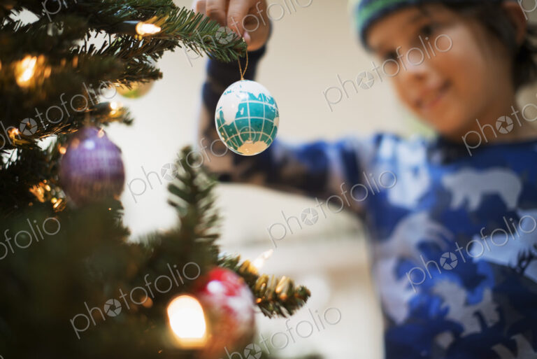 A young boy holding Christmas ornaments and placing them on the Christmas tree.