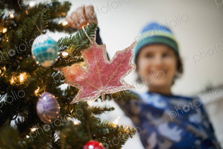 A young boy holding Christmas ornaments and placing them on the Christmas tree.