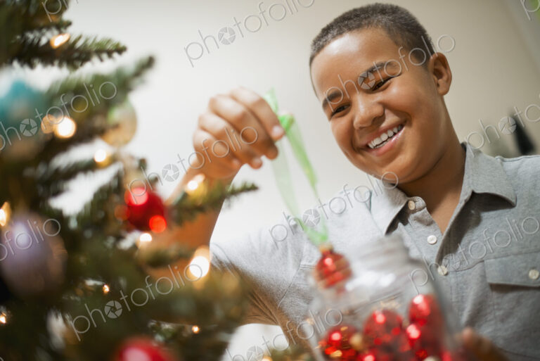A young boy holding Christmas ornaments and placing them on the Christmas tree.