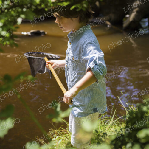 A young boy holding a fishing net, by a shallow river. Camping in the New Forest. A young boy holding a fishing net, by a shallow river. Camping in the New Forest.