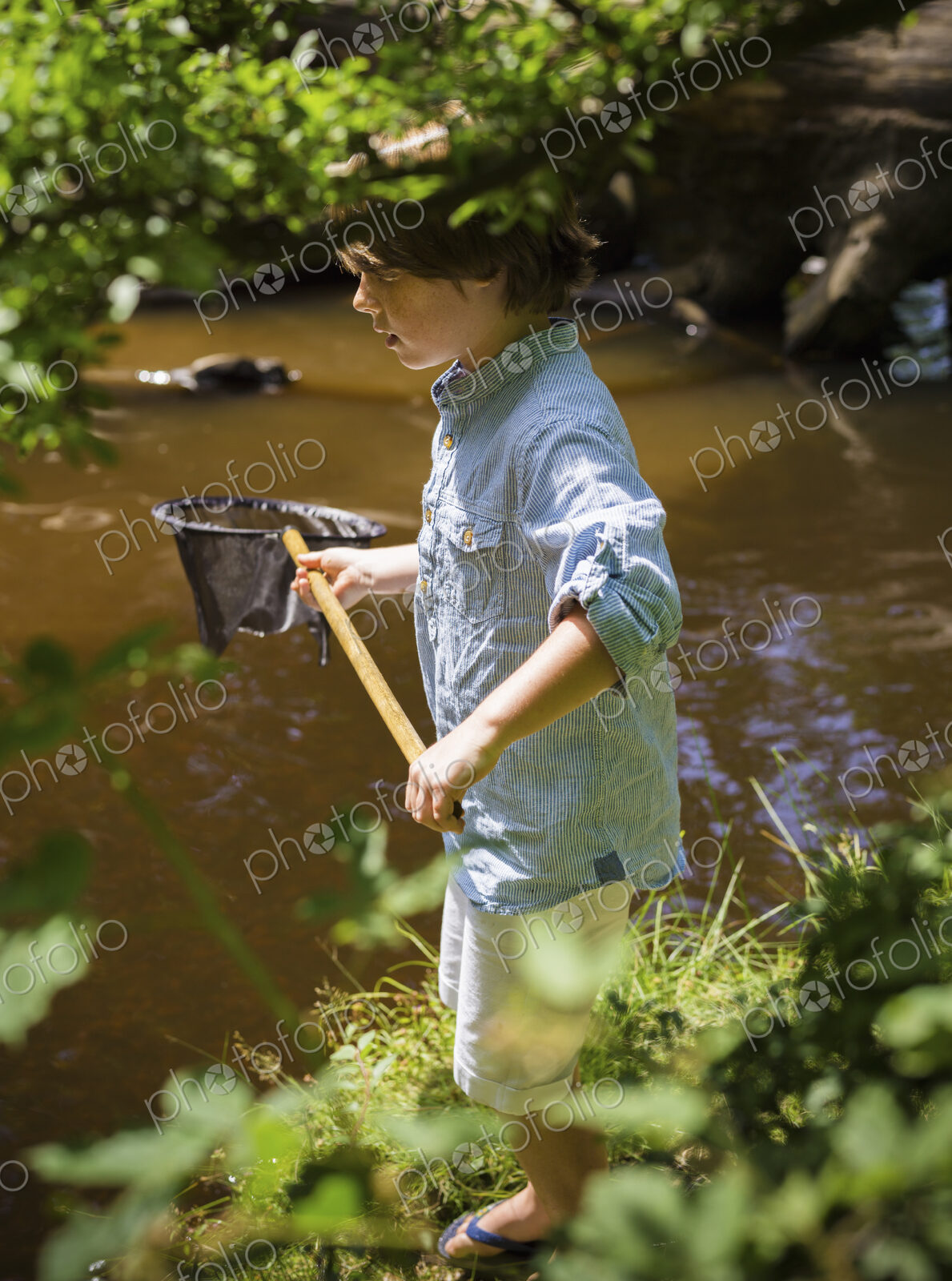 A young boy holding a fishing net, by a shallow river. Camping in the New Forest.