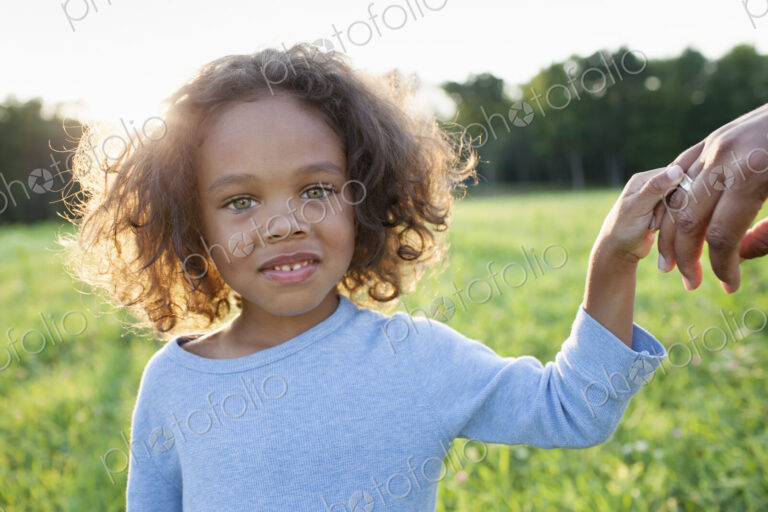 A young boy holding his mother's hand, standing in the grass in a field.