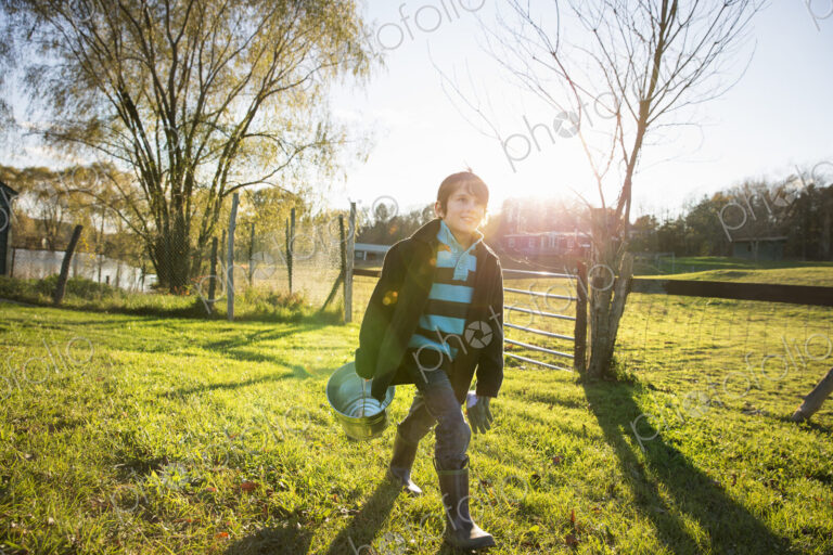 A young boy in an animal paddock, holding a bucket of feed. Animal sanctuary.