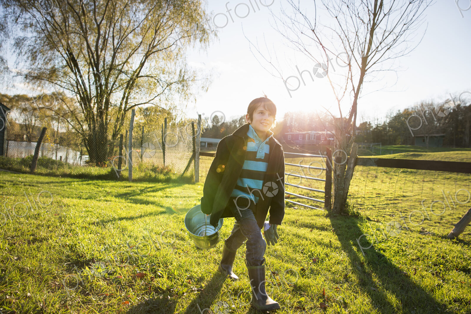 A young boy in an animal paddock, holding a bucket of feed. Animal sanctuary.