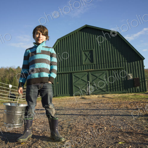 A young boy in an animal paddock, holding a bucket of feed. Animal sanctuary.