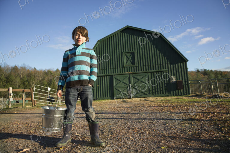 A young boy in an animal paddock, holding a bucket of feed. Animal sanctuary.