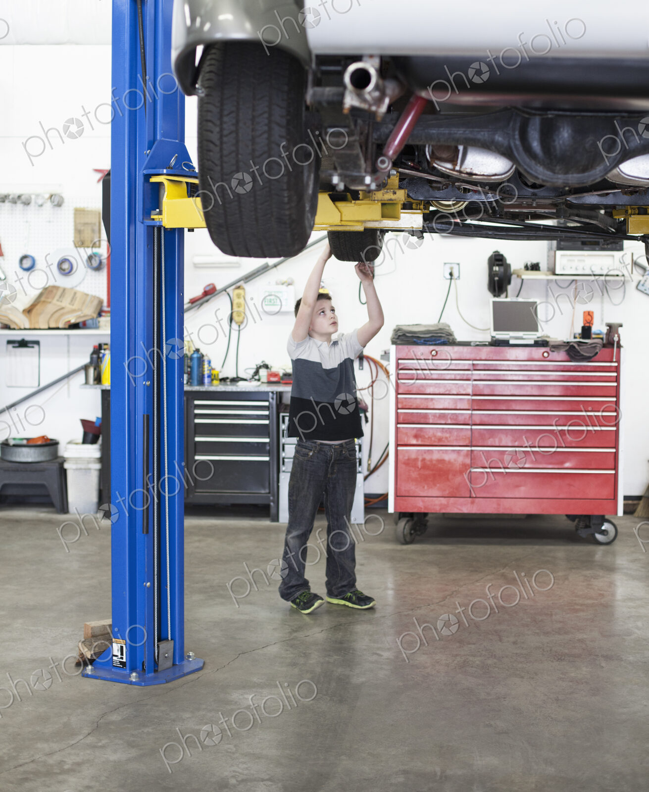 A young boy looks at a car tire in his dad’s classic car repair shop.