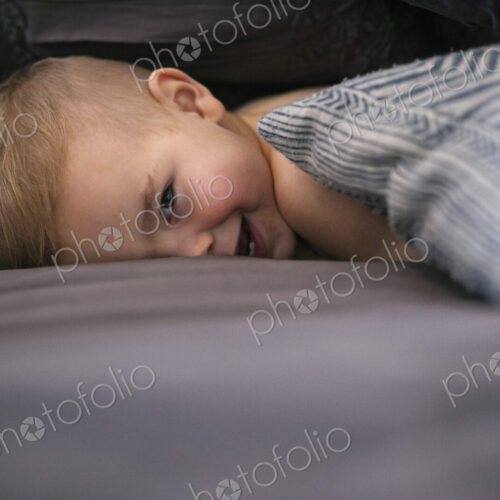 A young boy lying on his stomach in bed looking at the camera and laughing. A young boy lying on his stomach in bed looking at the camera and laughing.