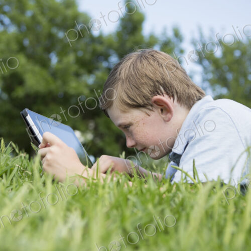 A young boy lying on the grass, using a digital tablet.