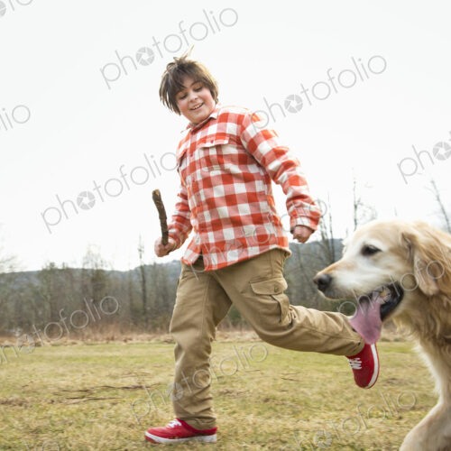 A young boy outdoors on a winter day, holding a stick and running with a golden… A young boy outdoors on a winter day, holding a stick and running with a golden…