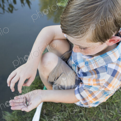A young boy outdoors sitting on a riverbank with a small fish in the palm of his hand. A young boy outdoors sitting on a riverbank with a small fish in the palm of his hand.
