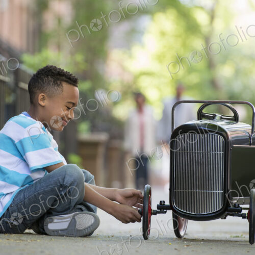A young boy playing with a old fashioned toy car on wheels on a city street. A young boy playing with a old fashioned toy car on wheels on a city street.