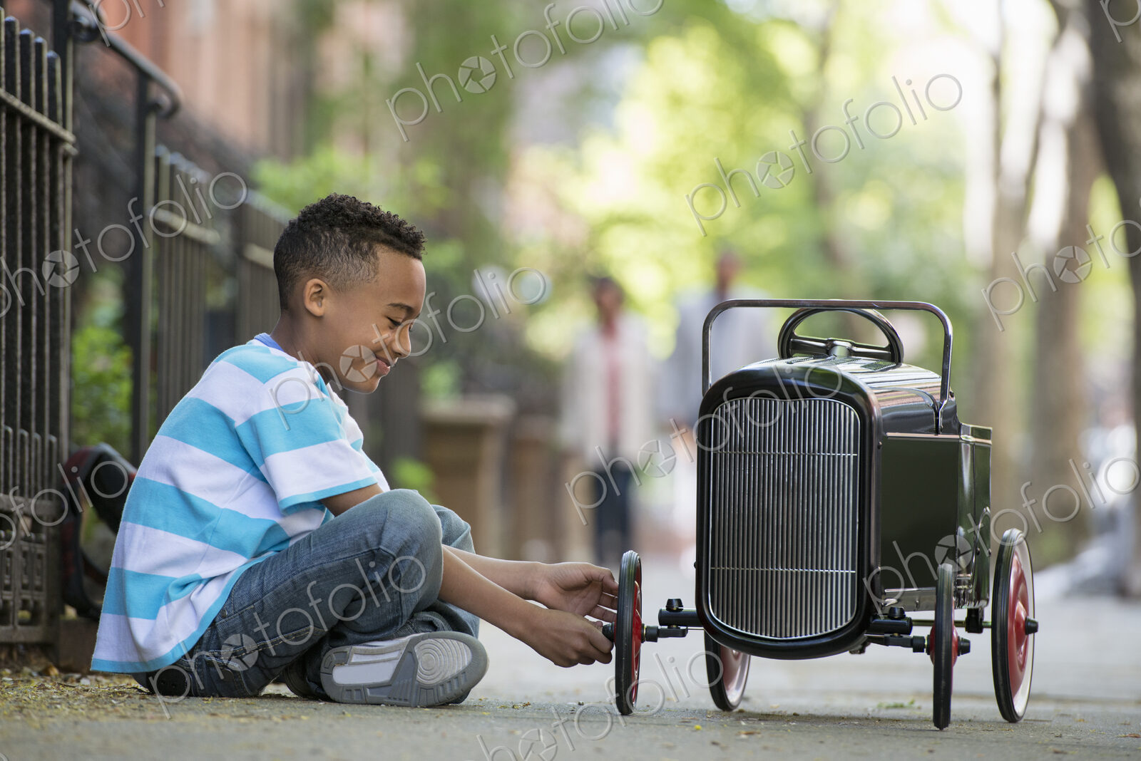 A young boy playing with a old fashioned toy car on wheels on a city street.