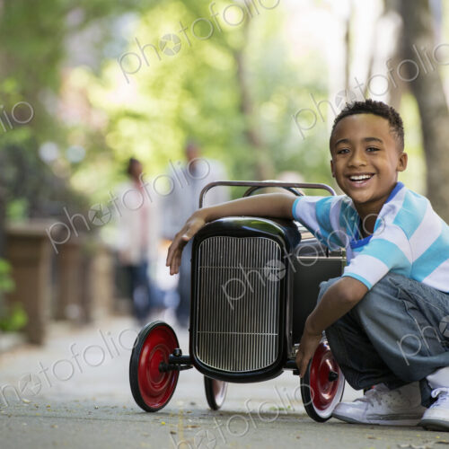 A young boy playing with a old fashioned toy car on wheels on a city street. A young boy playing with a old fashioned toy car on wheels on a city street.