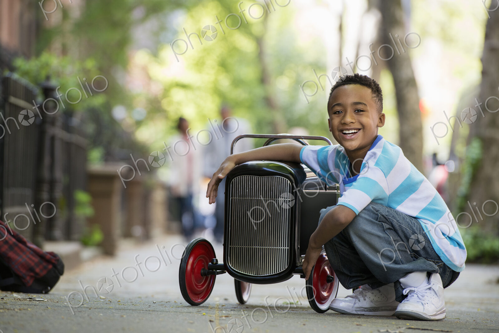 A young boy playing with a old fashioned toy car on wheels on a city street.