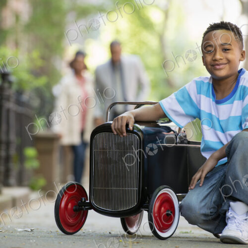 A young boy playing with a old fashioned toy car on wheels on a city street. A couple… A young boy playing with a old fashioned toy car on wheels on a city street. A couple…