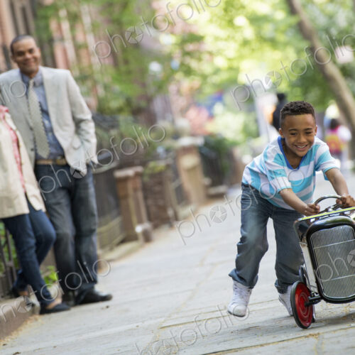 A young boy playing with a old fashioned toy car on wheels on a city street. A couple… A young boy playing with a old fashioned toy car on wheels on a city street. A couple…