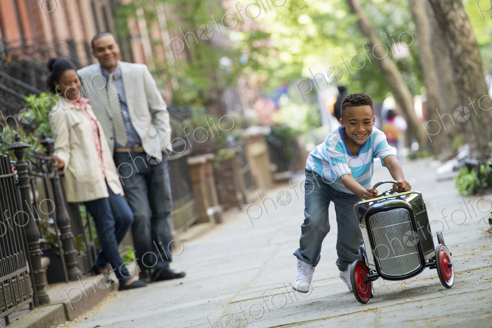 A young boy playing with a old fashioned toy car on wheels on a city street. A couple…