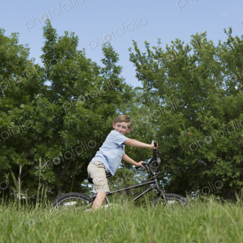 A young boy riding a bicycle through grass in a meadow.