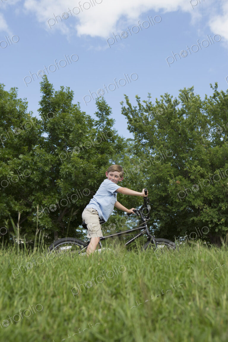 A young boy riding a bicycle through grass in a meadow.