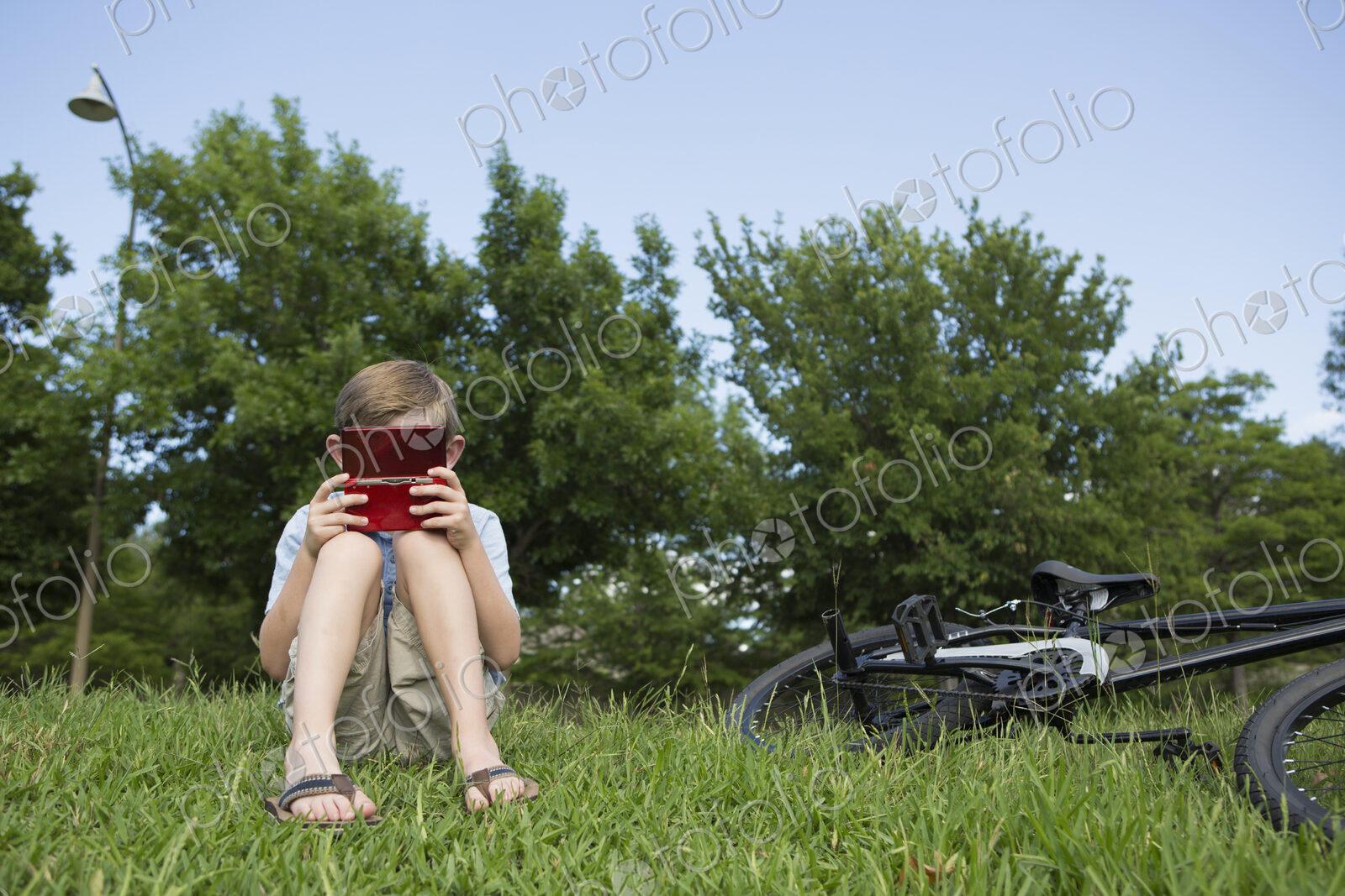 A young boy sitting on the grass playing a hand held electronic game.