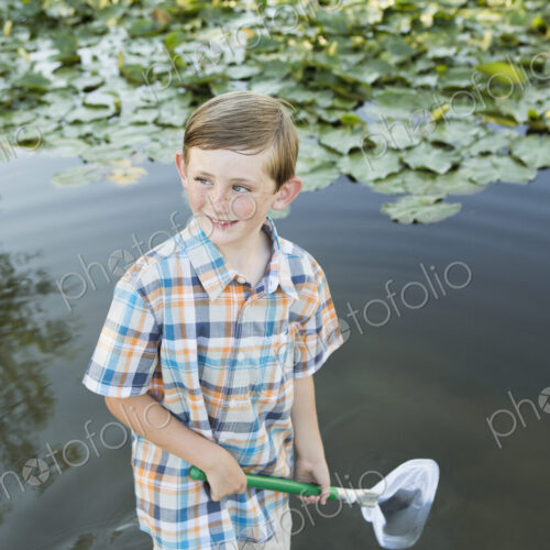 A young boy standing in shallow water with a fishing net.