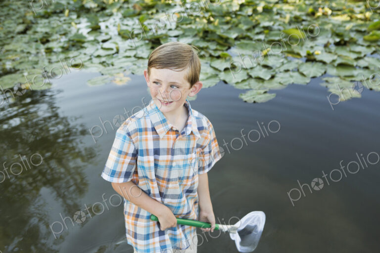 A young boy standing in shallow water with a fishing net.