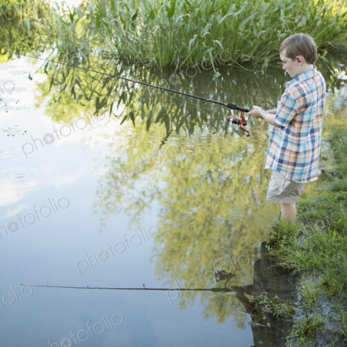 A young boy standing in water fishing with a rod. A young boy standing in water fishing with a rod.