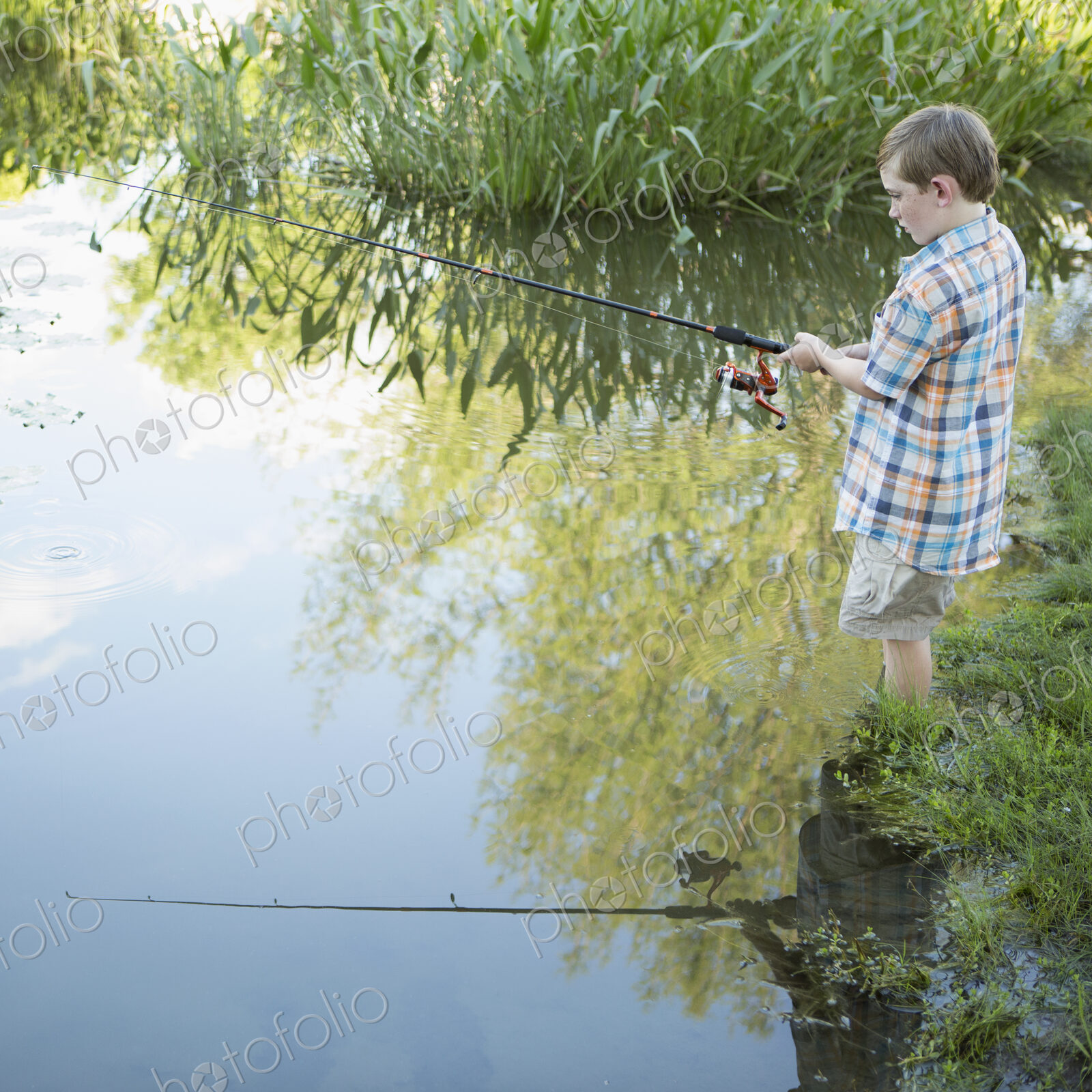 A young boy standing in water fishing with a rod.